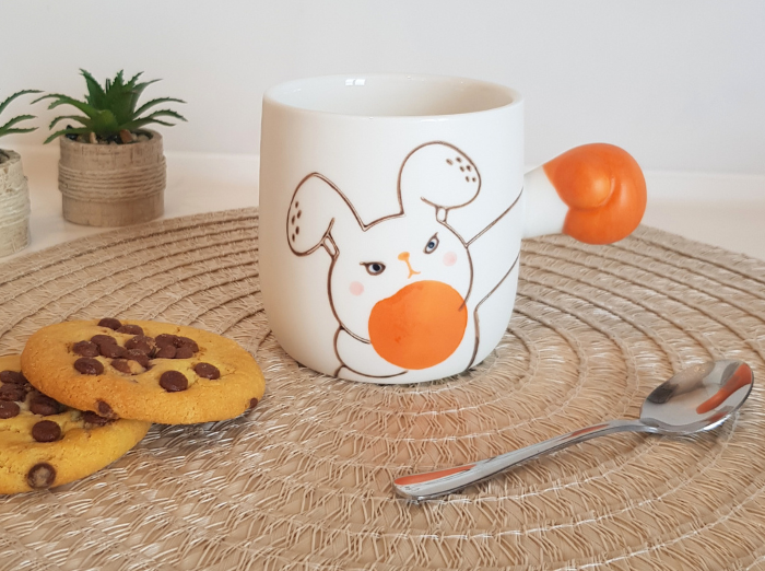 BOXING RABBIT MUG. A funny gift. White mug with a rabbit drawn on it and as a holder it has the arm of the rabbit extended, with an orange glove, as if it was boxing. Rabbit is looking angry.