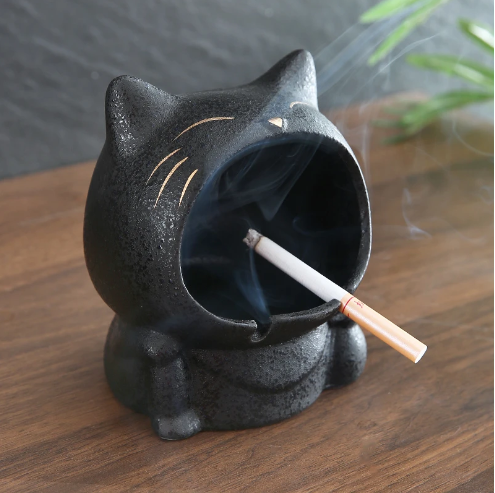 Big mouth cat ashtray on the table with a cigarette.