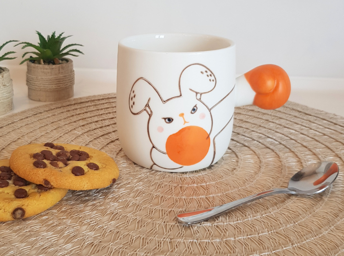 BOXING RABBIT MUG. A funny gift. White mug with a rabbit drawn on it and as a holder it has the arm of the rabbit extended, with an orange glove, as if it was boxing. Rabbit is looking angry. 